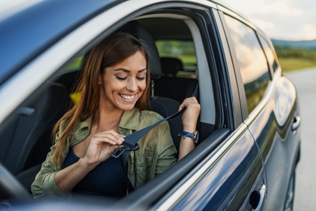 Woman in car putting on her seatbelt.