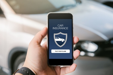 Accessing car insurance app on phone with car in the background